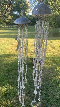 two silver chandeliers hanging from a tree in the grass with beads and other decorations