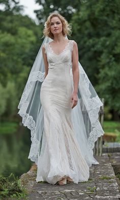 a woman in a wedding dress with a veil on her head is standing near the water