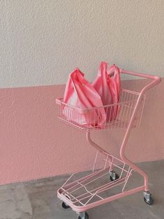 a pink shopping cart filled with bags on top of a cement floor next to a wall