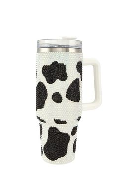 a white and black cow print coffee cup with handle on the side, in front of a