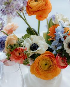 an arrangement of flowers in a white vase on a table with wine glasses and water