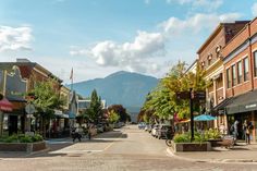 an empty street with shops and people walking on the sidewalks in front of mountains behind them