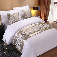 a bed with white and gold comforters in a bedroom next to a window,