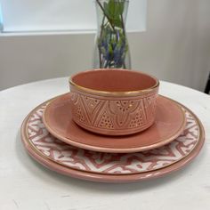 a set of pink and gold dinnerware on a white table with a vase in the background