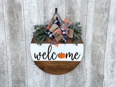 a welcome sign hanging on the side of a wooden fence with plaid bows and pumpkins