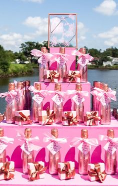 a pink cake with lots of bottles and bows on it sitting in front of the water