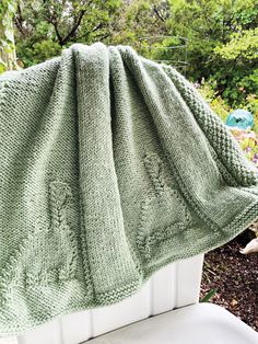 a green blanket sitting on top of a white chair next to flowers and trees in the background