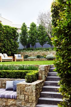 an outdoor seating area with stone walls and steps leading up to the grass covered lawn