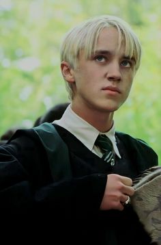 a young man with blonde hair wearing a harry potter outfit and holding a hogwarts tie