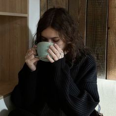 a woman sitting on a couch holding a coffee cup in her hands and looking down