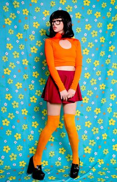 a woman in an orange top and red skirt posing for the camera with her hands on her hips