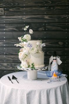 a white wedding cake sitting on top of a table next to a bottle of wine