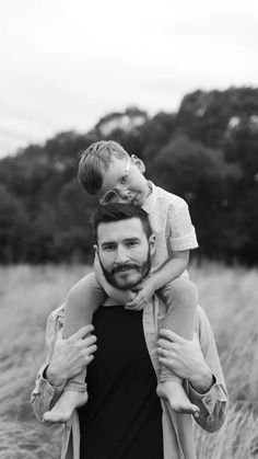 a man holding a little boy on his shoulders in the middle of an open field