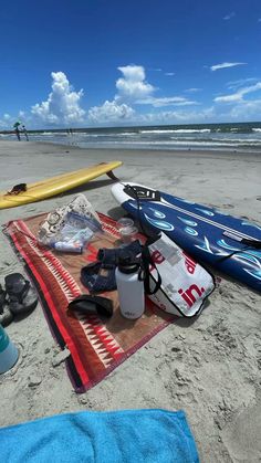 several surfboards are laying on the beach with towels and water bottles next to them