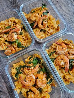 four plastic containers filled with pasta and shrimp on top of a wooden table next to vegetables