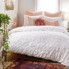 a bed with white comforter and pillows on top of it next to a potted plant