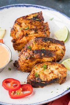 grilled chicken on a white plate with a side of dipping sauce and sliced red peppers