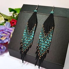 a pair of beaded earrings sitting on top of a black box next to flowers