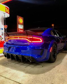 a blue sports car is parked in front of a gas station at night with the lights on