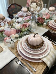 the table is set with pink and white plates, silverware, and pumpkins