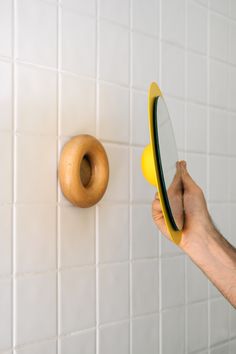 a hand holding a yellow mirror next to a doughnut on a white tiled wall