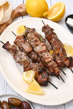 a plate with skewered meat and lemons on it next to olives