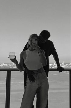 a man standing next to a woman holding a glass of wine on top of a balcony