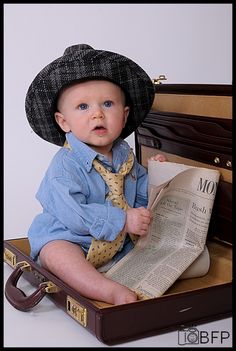 a baby sitting in a suit case with a hat and tie on it's head