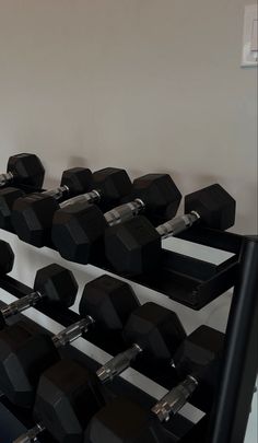 there are many black dumbs on the rack in this gym room with white walls