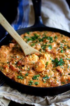 a skillet filled with shrimp and sauce on top of a cloth next to a wooden spoon