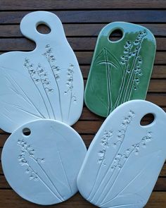 four white and green ceramic cutting boards with flowers on them sitting on a wooden surface