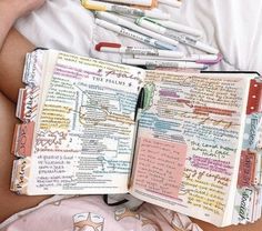 a person laying in bed with an open book and several pens on top of it