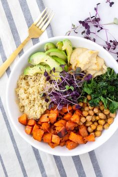 a white bowl filled with different types of food next to a fork and knife on a striped table cloth