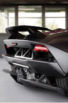 the rear end of a black sports car parked in a garage with lots of windows