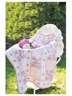 a pink and white crocheted blanket sitting on top of a chair in the grass