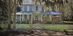 a white house with trees in front of it and a picket fence around the yard