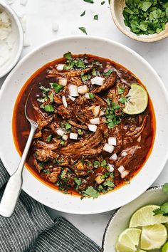 a white bowl filled with beef and onions next to two bowls of cilantro