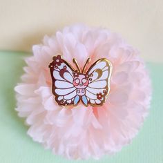 a butterfly brooch sitting on top of a pink flower