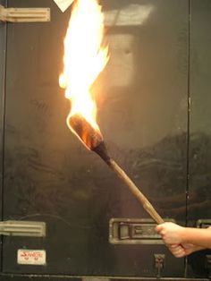 a person holding a long stick with flames coming out of it in front of an oven