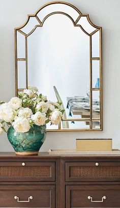 a vase filled with white flowers sitting on top of a dresser next to a mirror