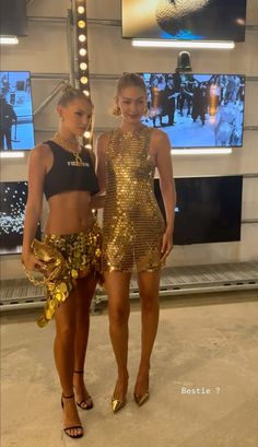 two women standing next to each other in front of a tv screen and wearing gold sequins