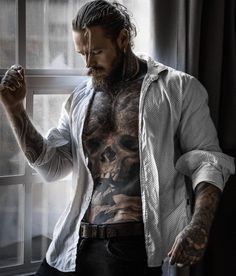 a man with tattoos standing in front of a window