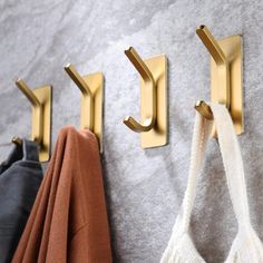 three coat hooks are hanging on the wall next to two sweaters and one bag