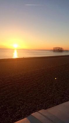 the sun is setting over the beach and pier