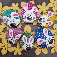 four painted rocks with animals on them sitting in front of yellow and white flower petals