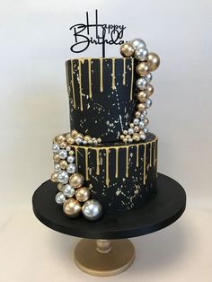 a black and gold birthday cake with pearls on the bottom tier is decorated with a happy birthday sign