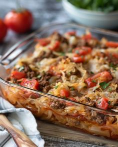 a casserole dish with meat and vegetables in it on a wooden table next to tomatoes