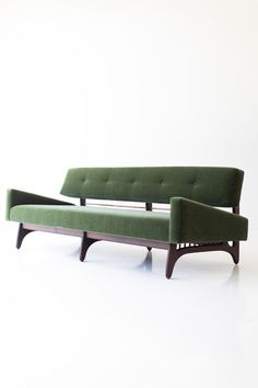 a green couch sitting on top of a white floor next to a wooden frame chair