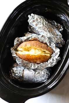 an open crock pot filled with potatoes and wrapped in foil