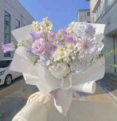 a person holding a bouquet of flowers in front of a building with cars parked on the street